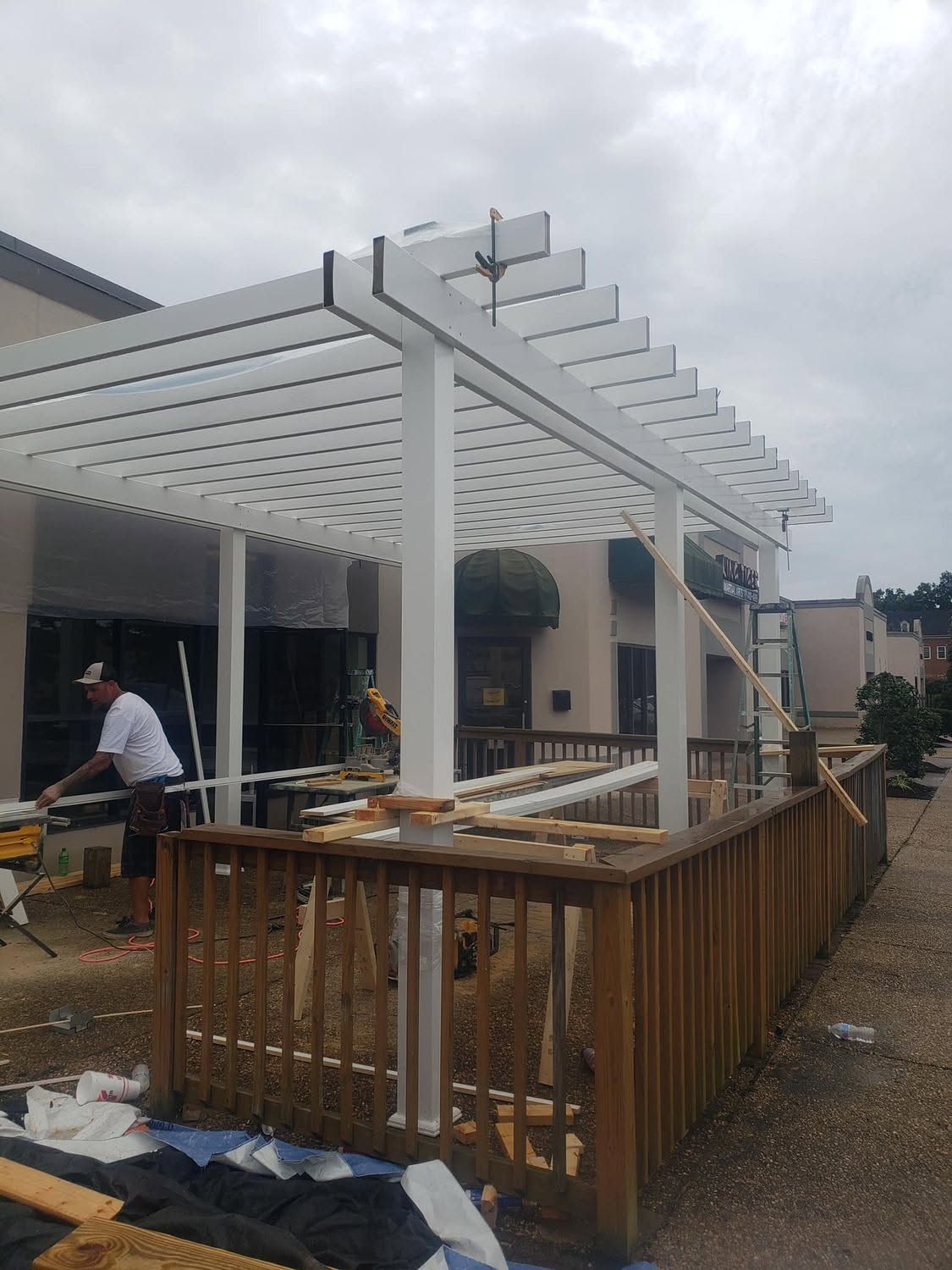 Backyard patio under construction with white pergola framing and wooden railing in front