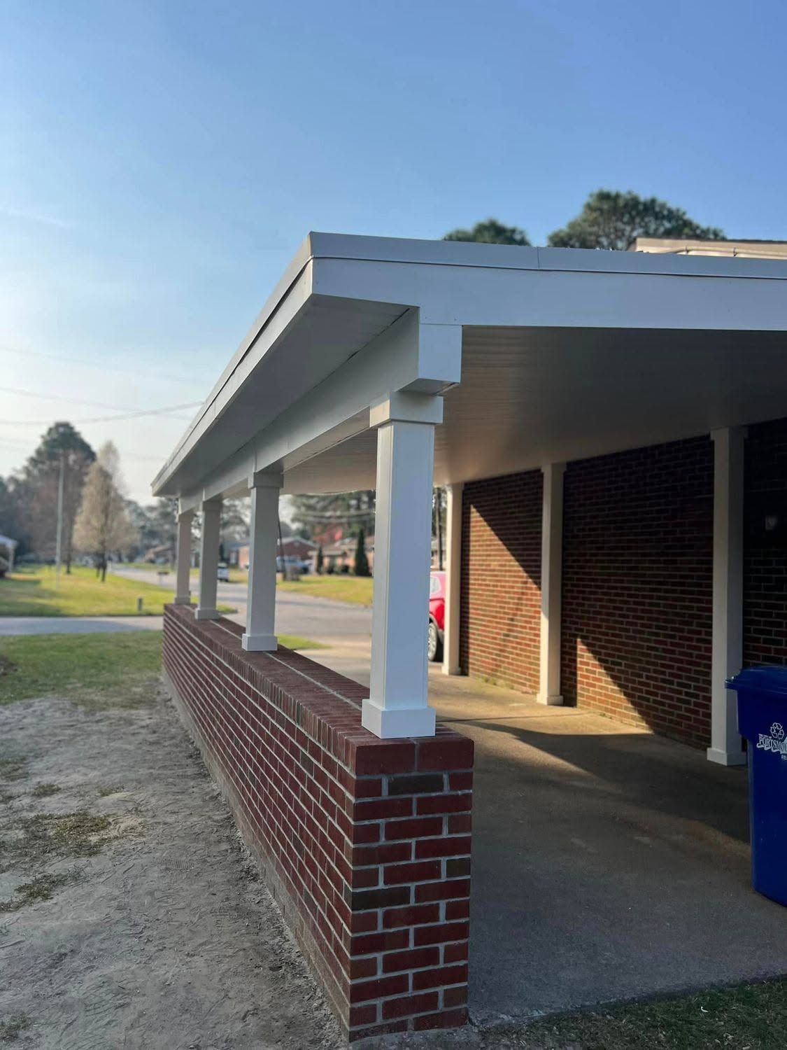 Brick-and-white covered porch beside a grassy field on a sunny day