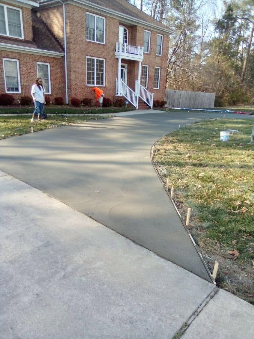 Curved driveway beside a brick house, with a person standing near the front steps.