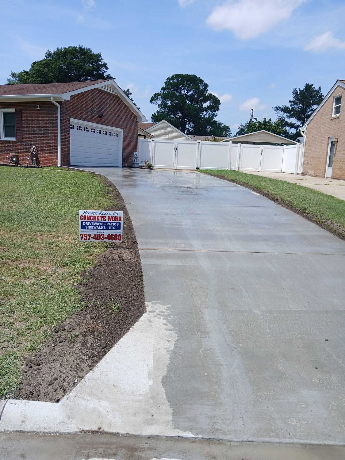 Steep concrete driveway beside brick garages and a white fence on a residential hill