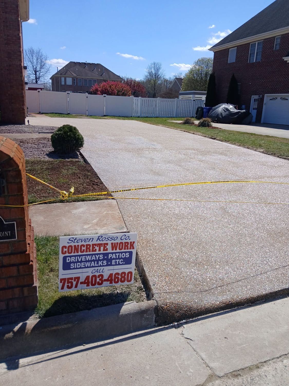 Driveway with wet concrete and a sidewalk sign advertising concrete work in a suburban yard.
