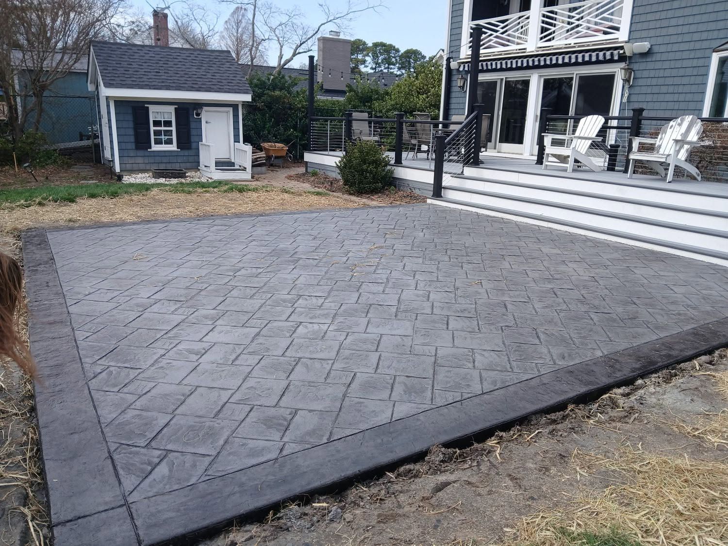 Stamped concrete patio in a backyard beside a white house and porch, with a small shed nearby.