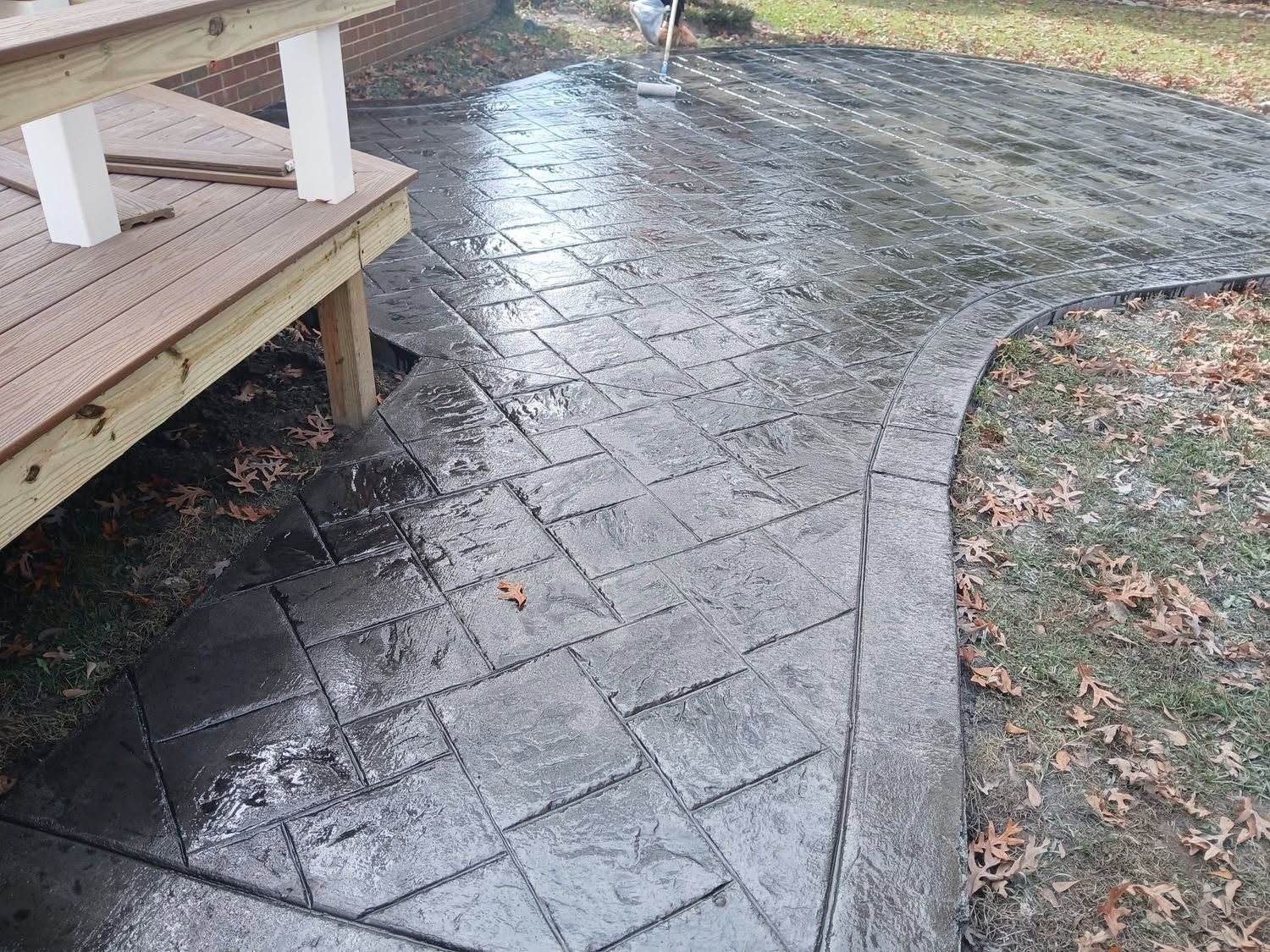 Wet brick patio beside a wooden porch, with leaves scattered along the curved walkway.