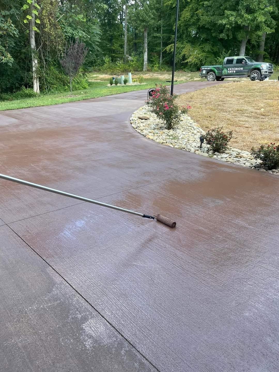 Wet concrete driveway curving past shrubs, with a parked truck in the background.