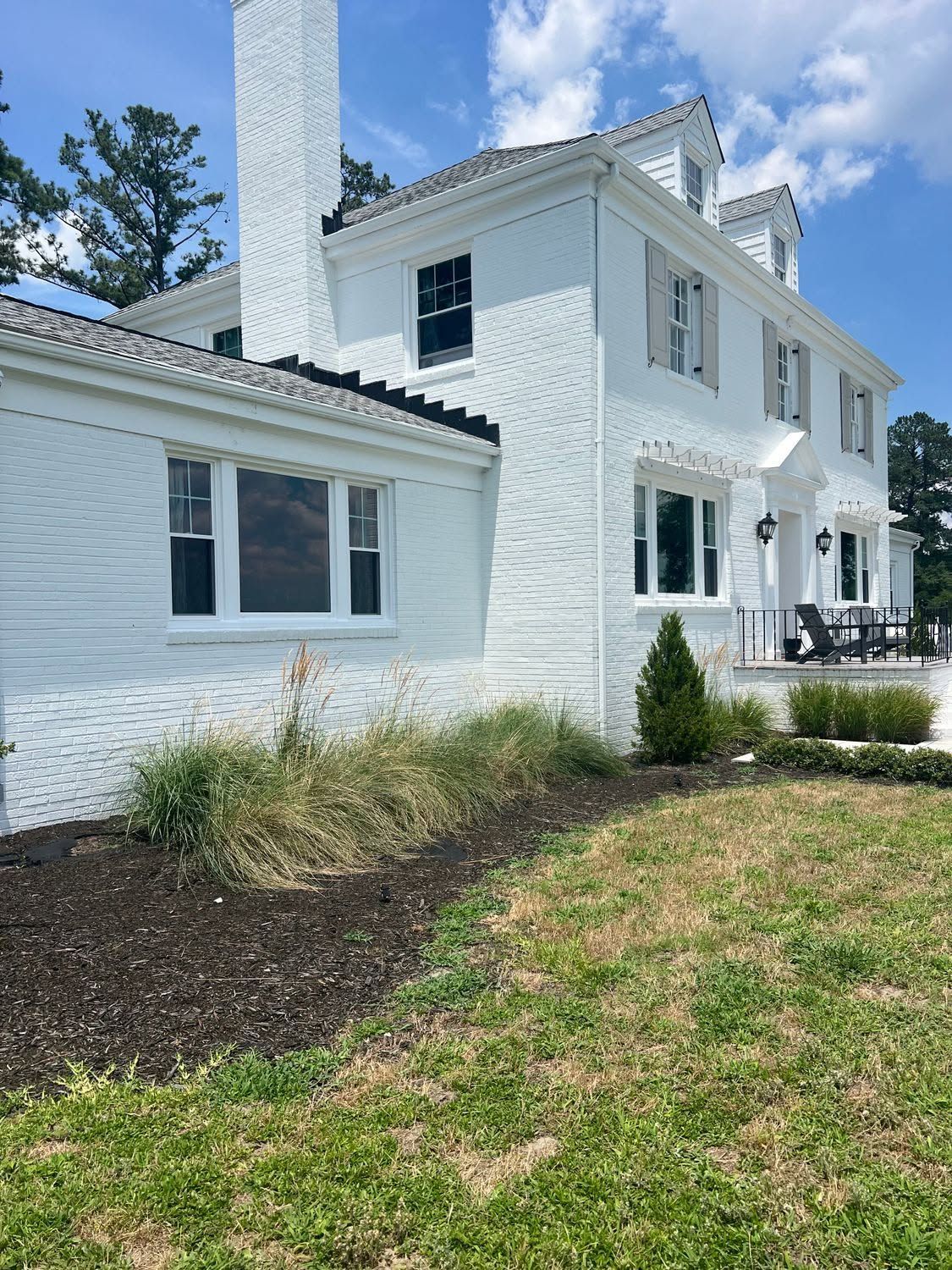 White two-story house with white siding, windows, and a chimney, viewed from a grassy yard