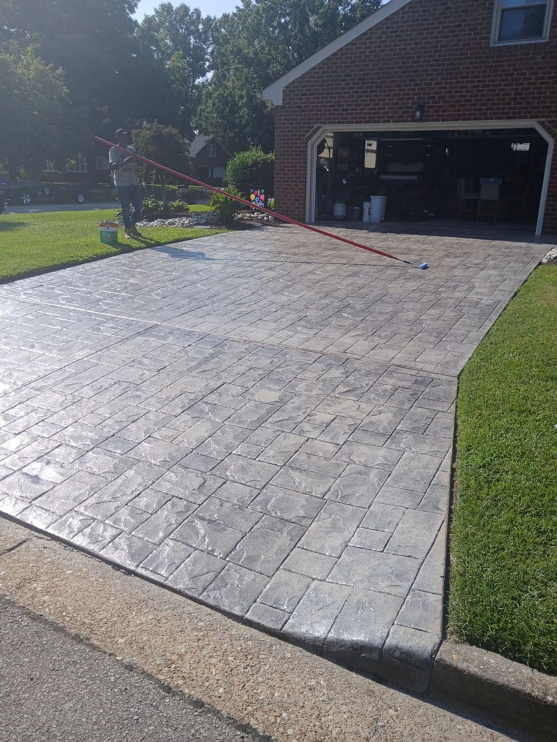Stamped concrete driveway leading to an open garage beside a brick house, with a grassy lawn.