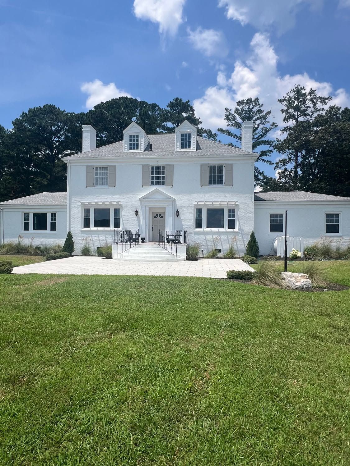 White colonial-style house with dormer windows, front porch, and green lawn under a blue sky
