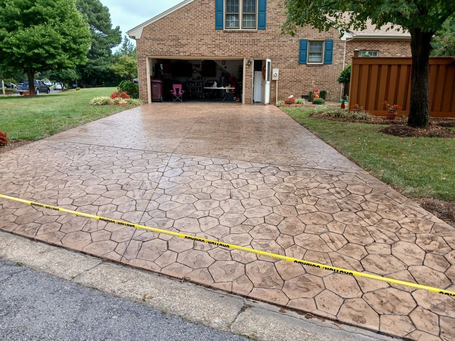 Cracked concrete driveway sloping to a brick house garage, with a yellow tape across the front.