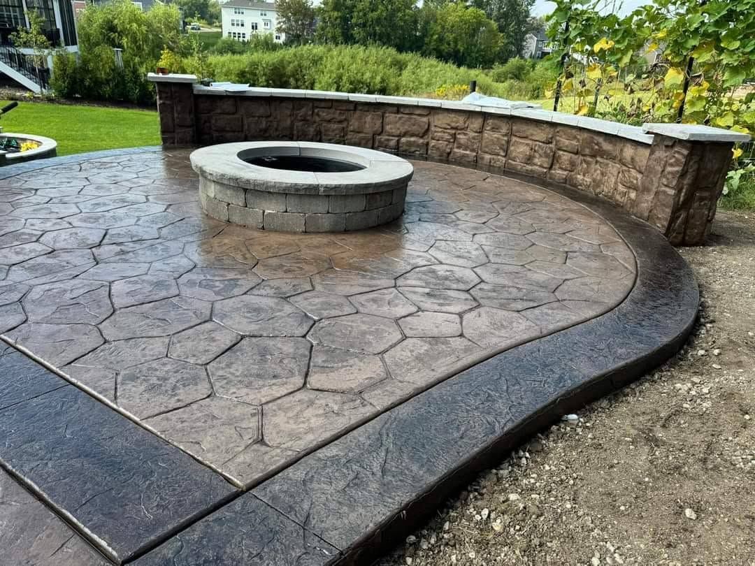 Circular stone fire pit with curved retaining wall on a stamped concrete patio in a garden setting