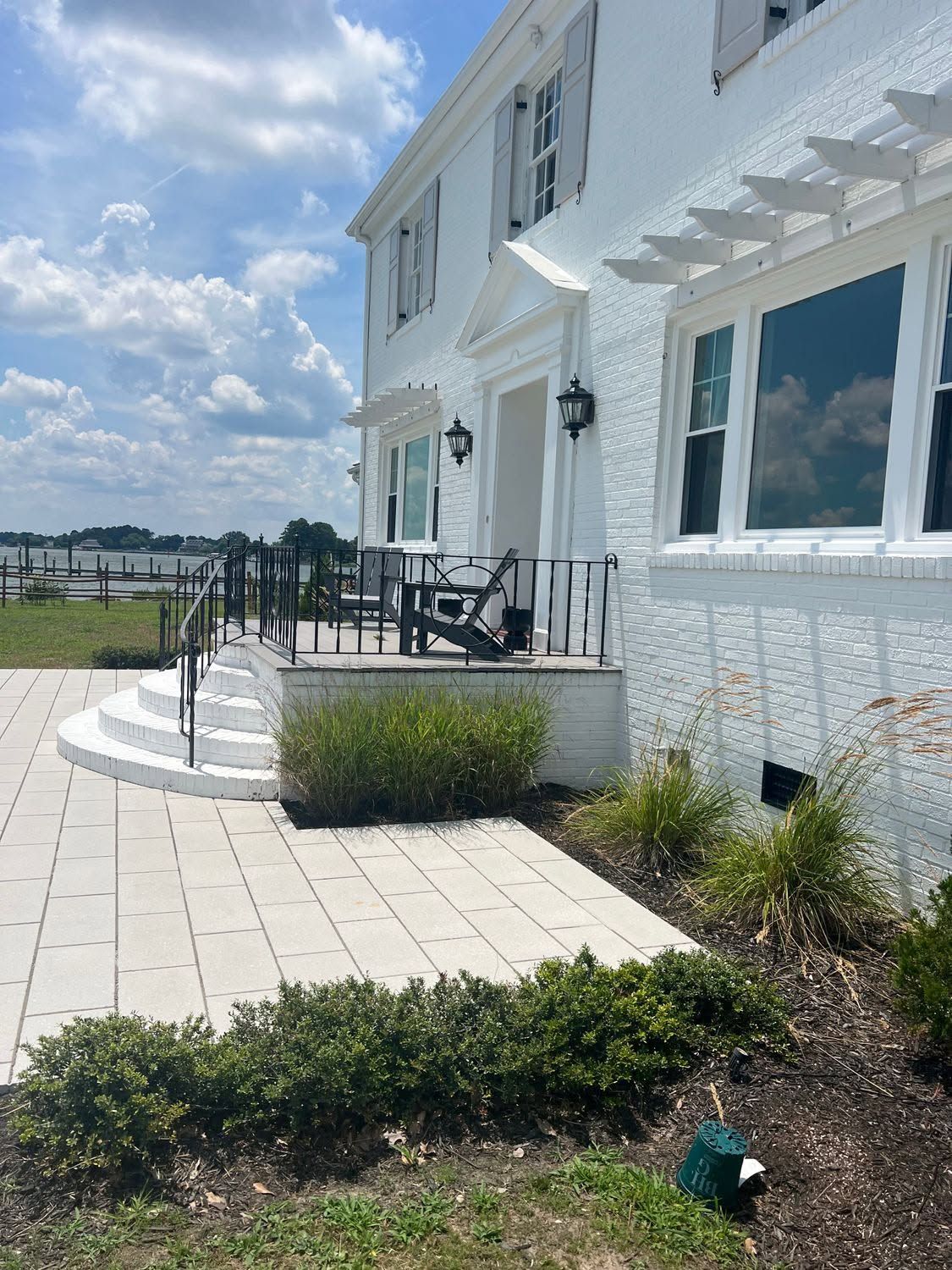 White waterfront house patio with black chairs, glass railing, and landscaped garden under a cloudy sky