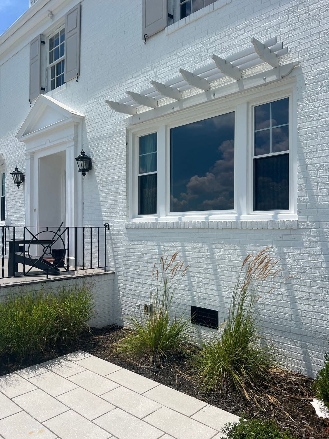 White townhouse exterior with blue shutters, black lanterns, patio chairs, and a small front garden