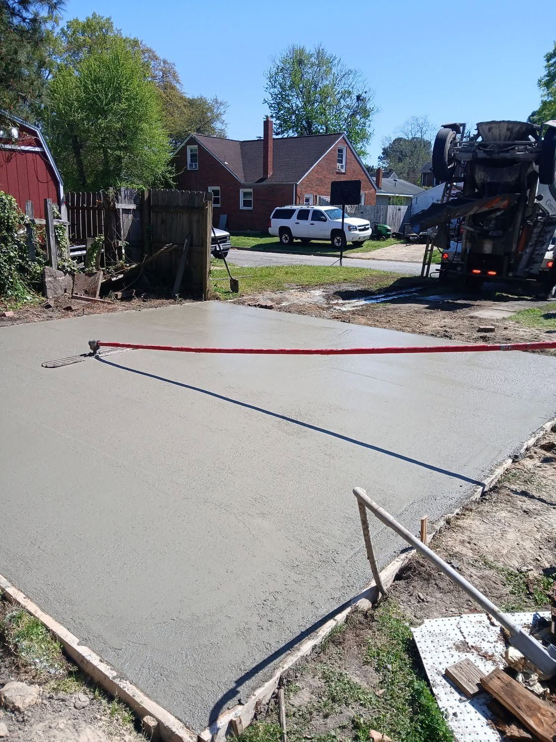 Concrete driveway slab being poured in a residential yard, with red leveling line and construction equipment nearby