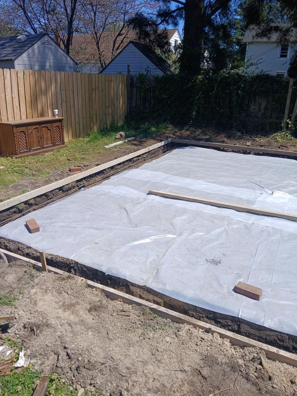 Backyard with a freshly covered rectangular concrete slab framed by wood boards and plastic sheeting