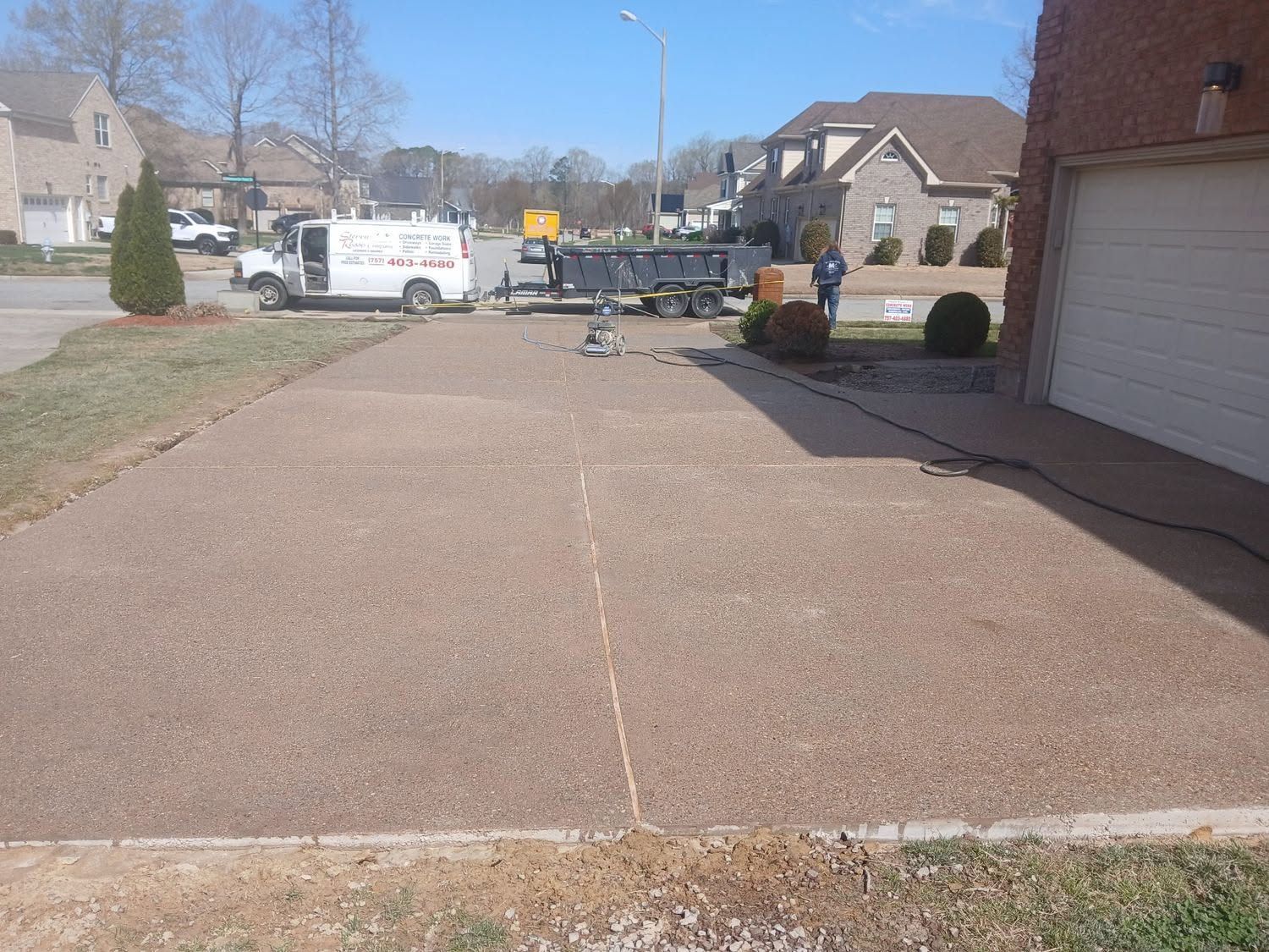 Driveway with a white utility truck, trailer, and workers near a house on a sunny day.
