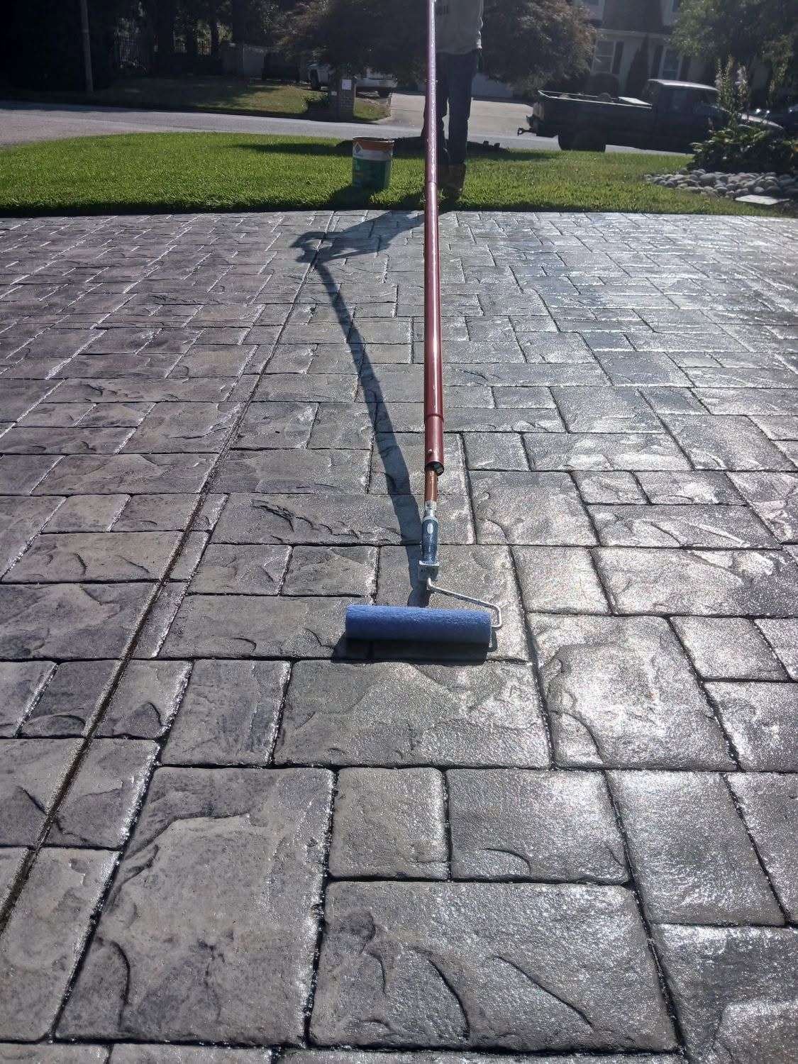 Blue-handled broom standing on a paved patio in a sunny yard