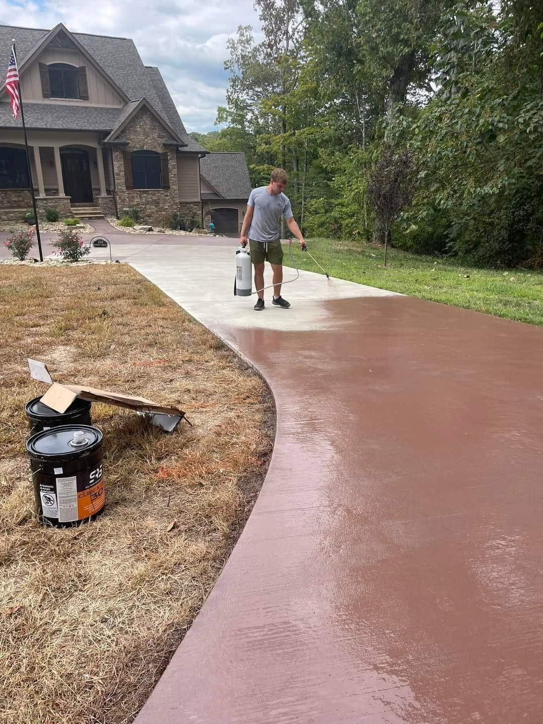 Person power-washing a curved concrete driveway beside a house and lawn.