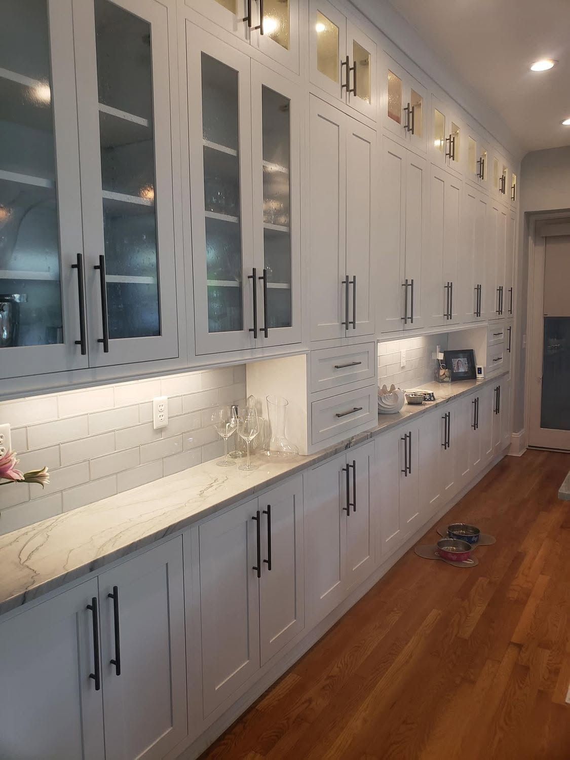 Modern kitchen with light blue cabinets, white countertops, tile backsplash, and warm wood floors.