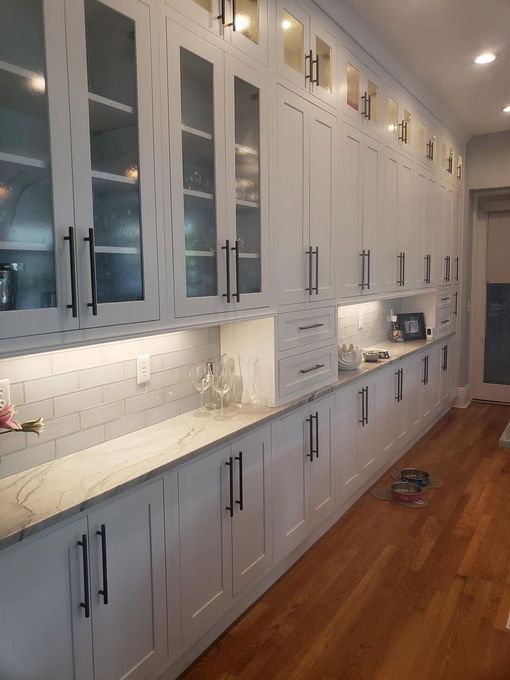 Bright white kitchen with tall cabinets, marble countertop, under-cabinet lighting, and hardwood floors.