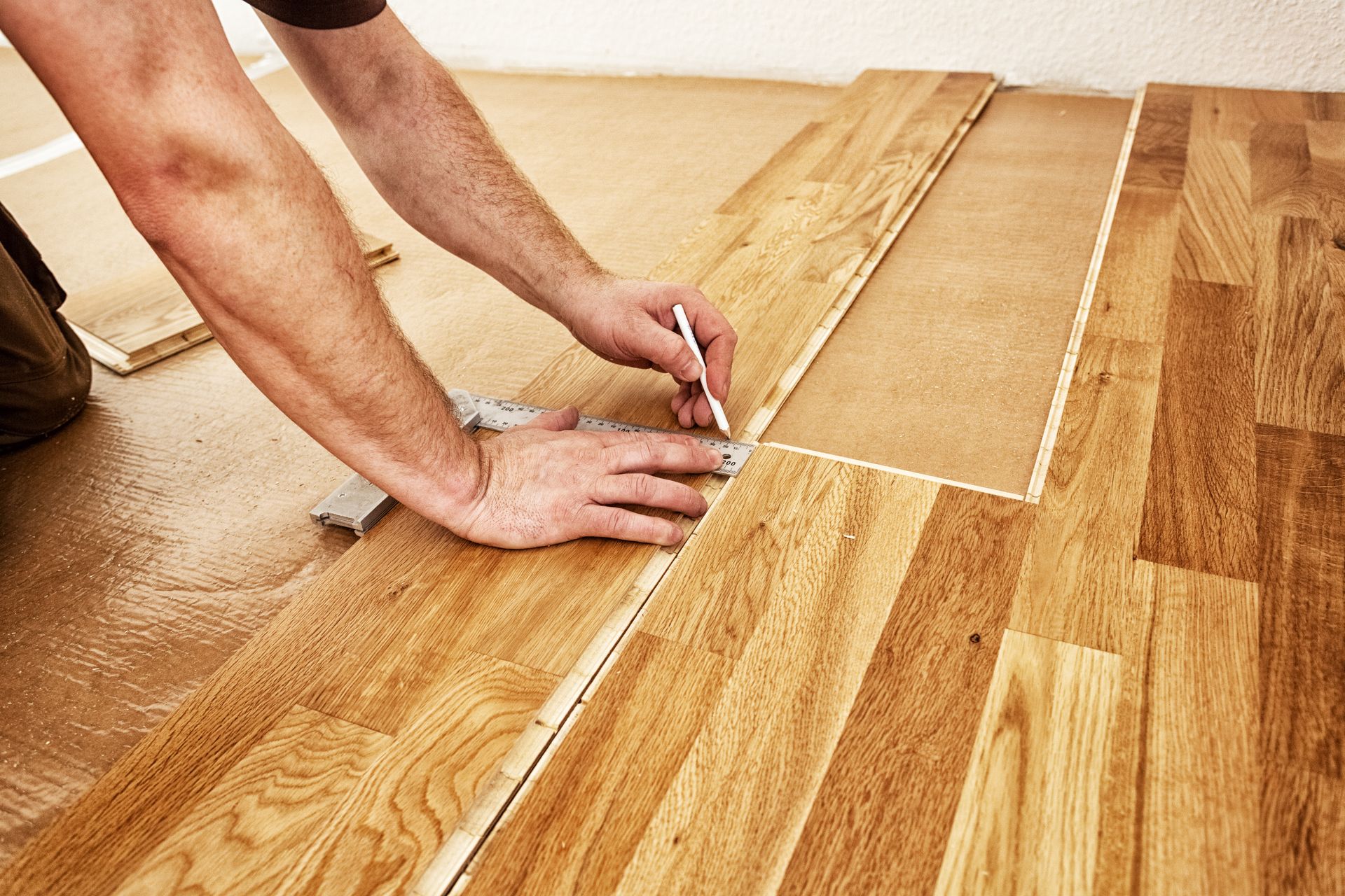 Hands installing wood flooring with a tool on a light oak floor.