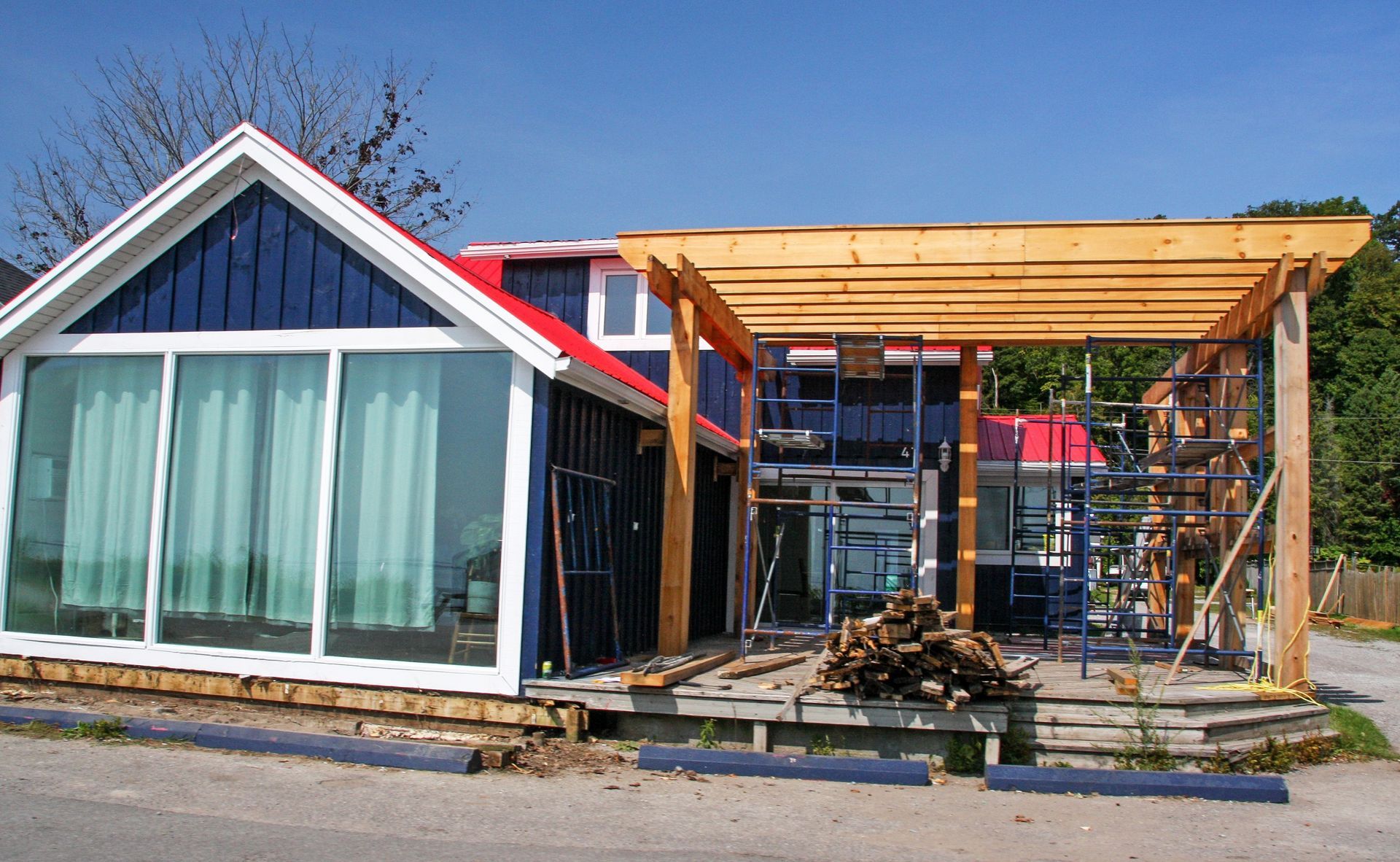 Small house under construction with large front windows and a wooden pergola frame.