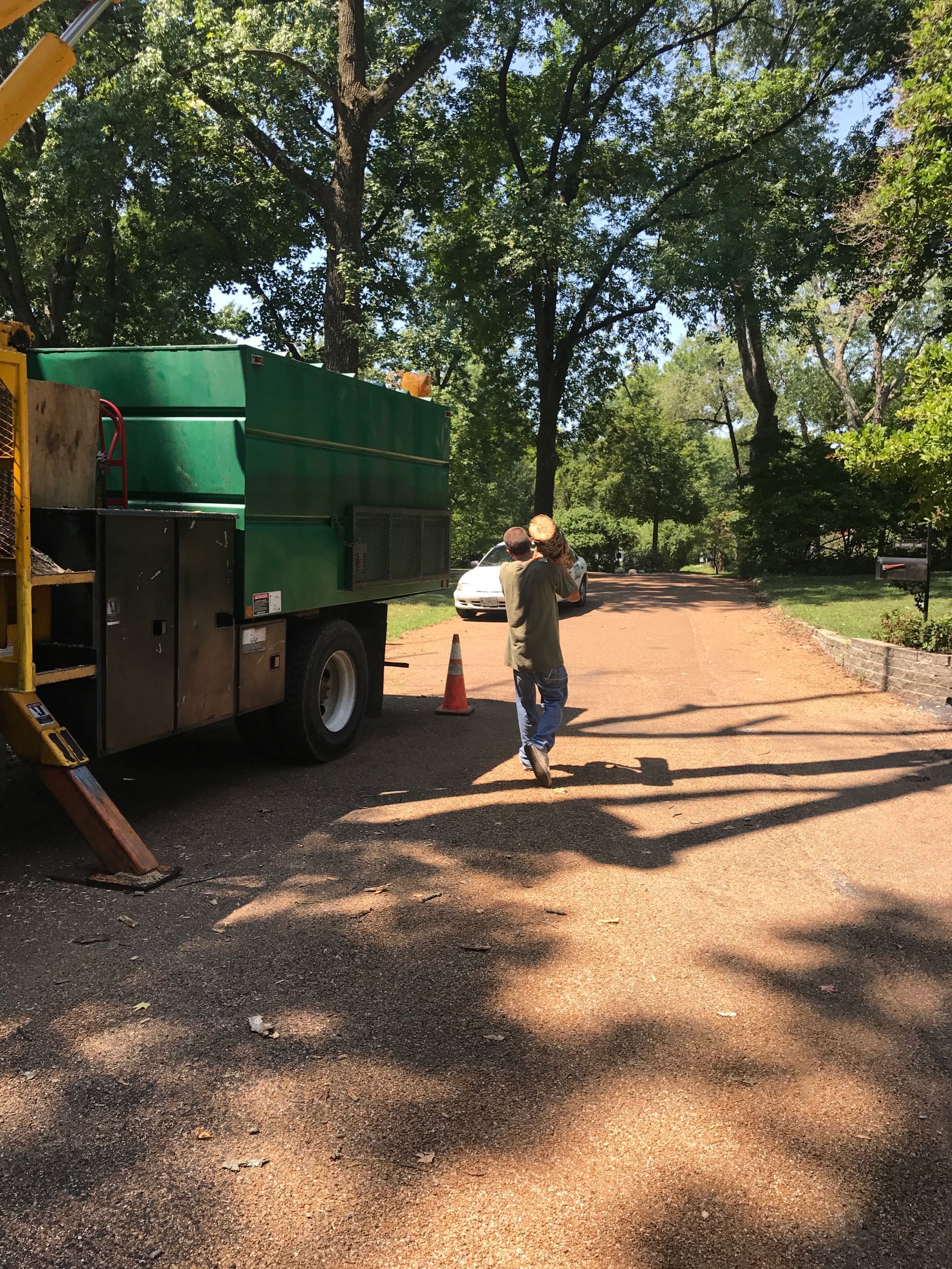 Green utility truck and worker on a gravel path in a wooded park.