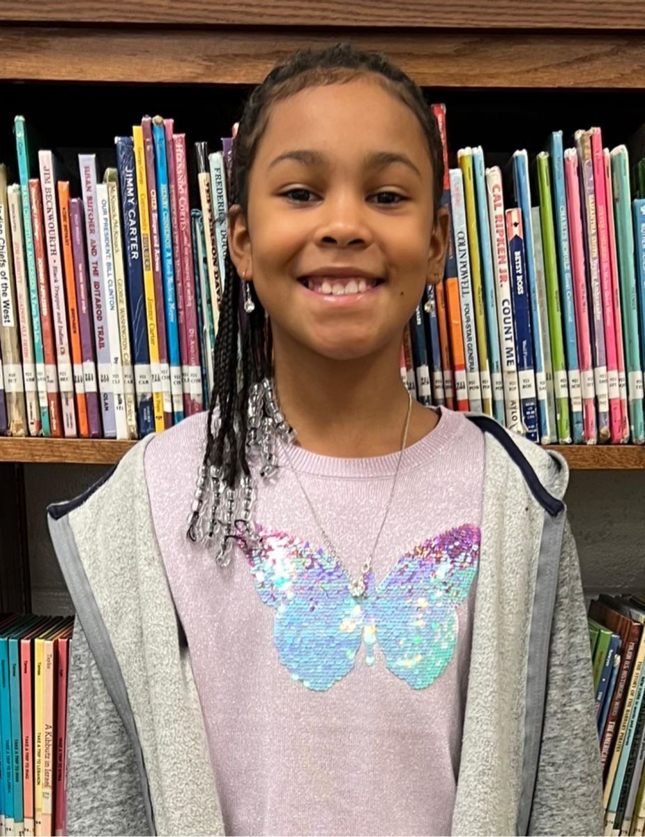 a young girl is smiling in front of a bookshelf filled with books .
