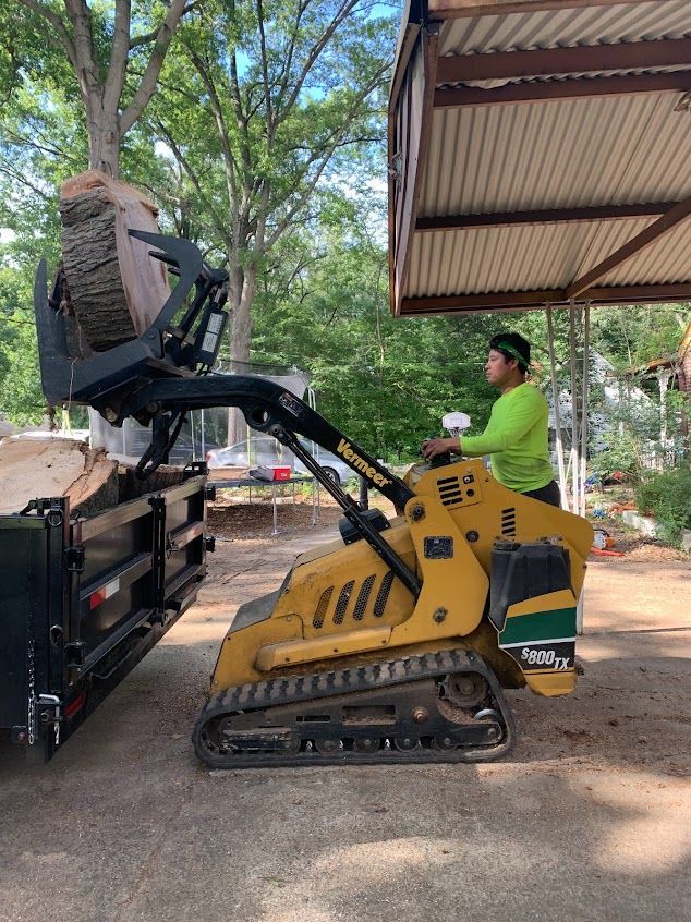 Worker operating a yellow skid steer to lift a large tire onto a truck under a shed