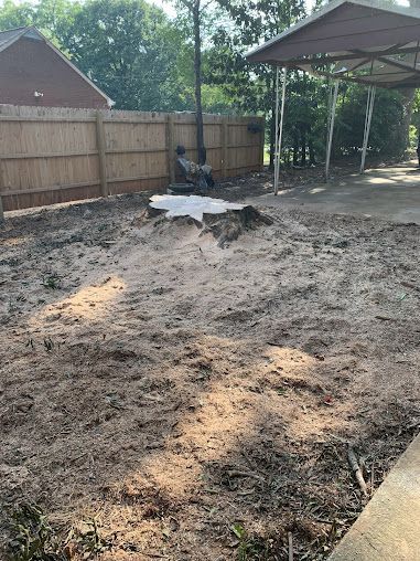 Backyard with freshly dug, muddy ground, a wooden fence, and a covered patio area.
