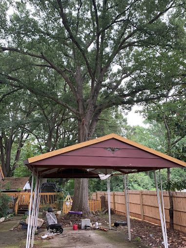 Backyard gazebo with maroon roof under tall trees, surrounded by wooden fencing and yard clutter
