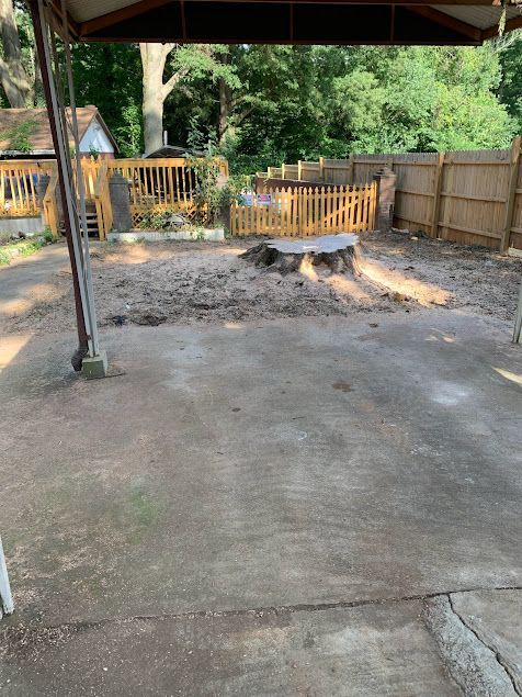 Empty concrete patio with a small fenced fire pit area and trees in the backyard.