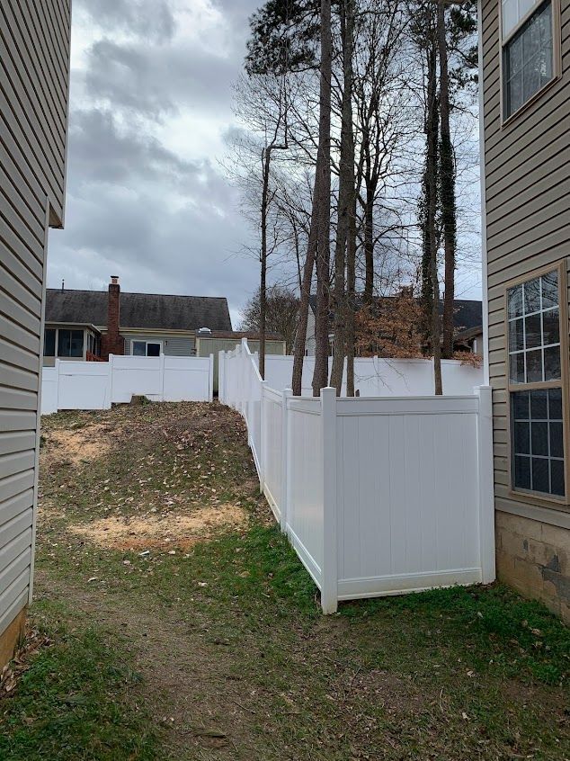 Narrow grassy side yard between houses with a white fence and a small white utility enclosure under bare trees