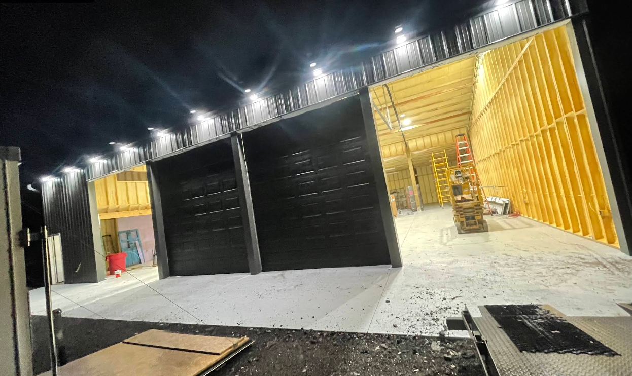 Nighttime view of a lit warehouse with black garage doors and a bright yellow open bay.
