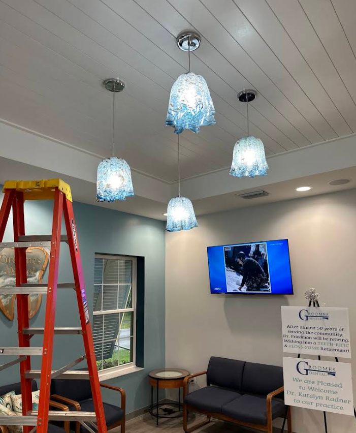 Indoor waiting room with blue hanging lights, a red ladder, wall TV, and a couch