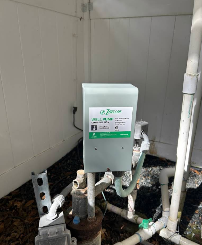 Grey utility box with pipes and valves in a tiled industrial corner outdoors