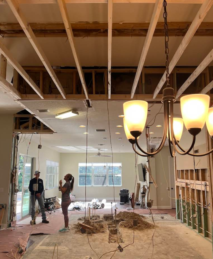 Partially renovated room with exposed ceiling beams, hanging lights, and two workers near the back wall.