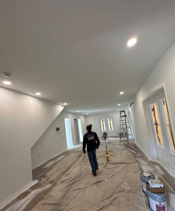 Workers renovating a bright white room with drop cloths, ladders, and recessed ceiling lights