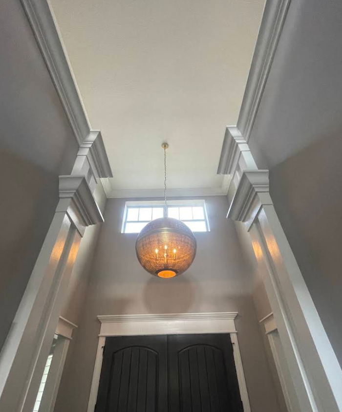 Grand entryway with tall gray walls, hanging globe chandelier, and dark double doors under a high ceiling.