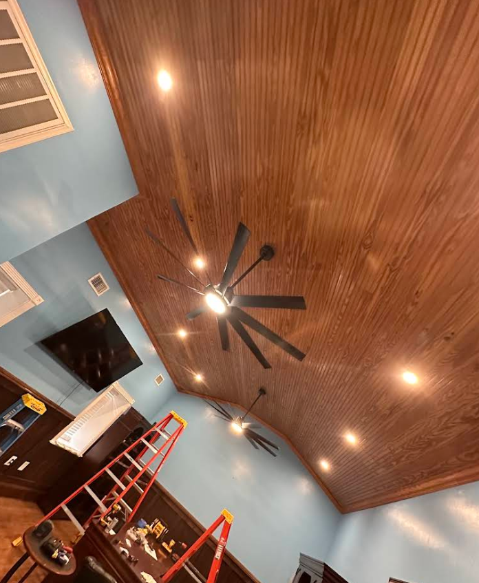Tilted view of a room with wood-paneled ceiling, ceiling fans, recessed lights, and ladders in a blue-walled interior