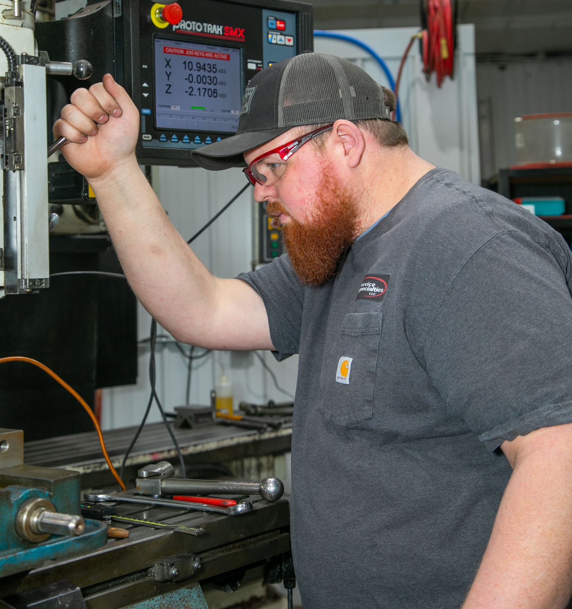 Technician operating a machine in a workshop, using a hand lever beside a digital control panel.
