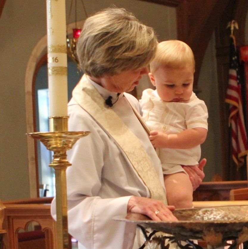 A woman is holding a baby in front of a candle with the number 16 on it