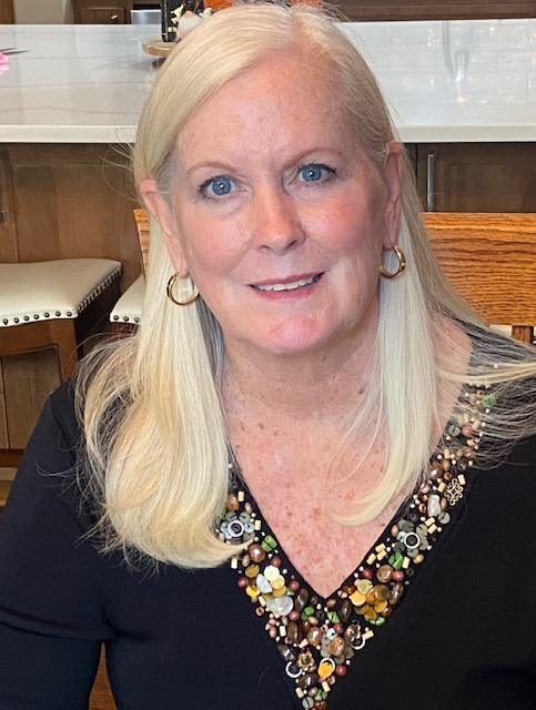 A woman wearing sunglasses is smiling with her hand on her chin