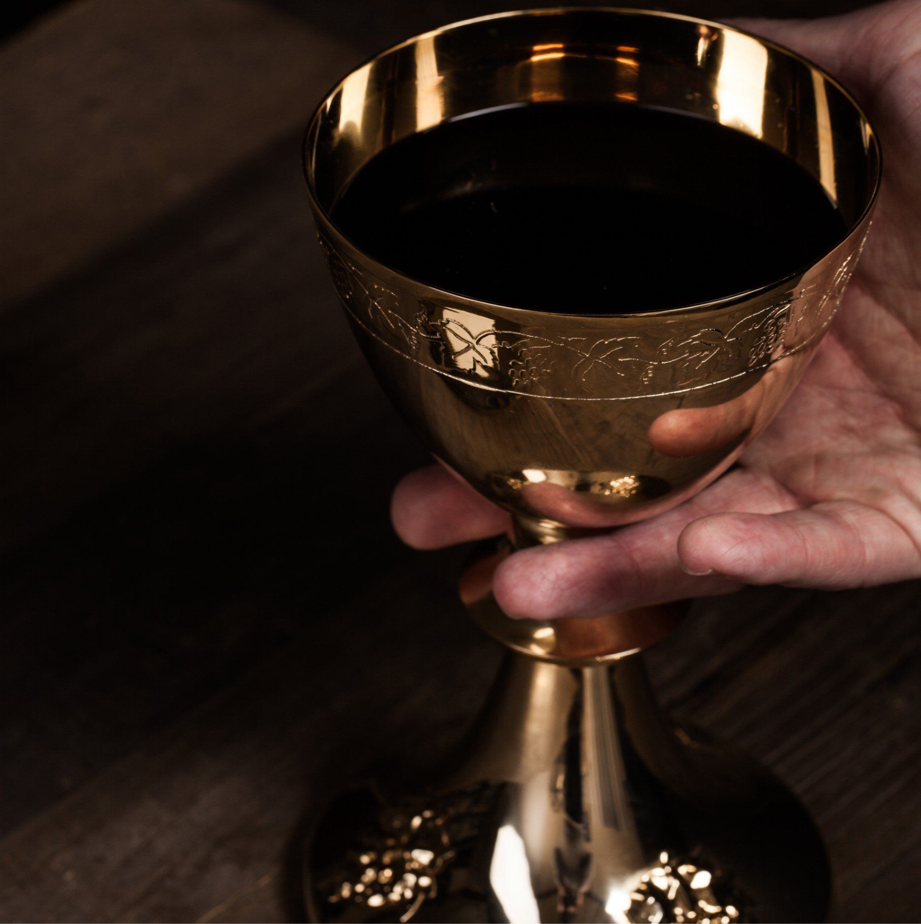 A person is holding a gold chalice with a black liquid in it