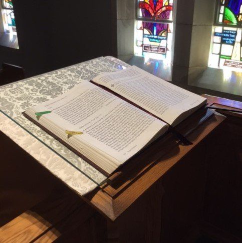 A bible is open on a podium in front of a stained glass window