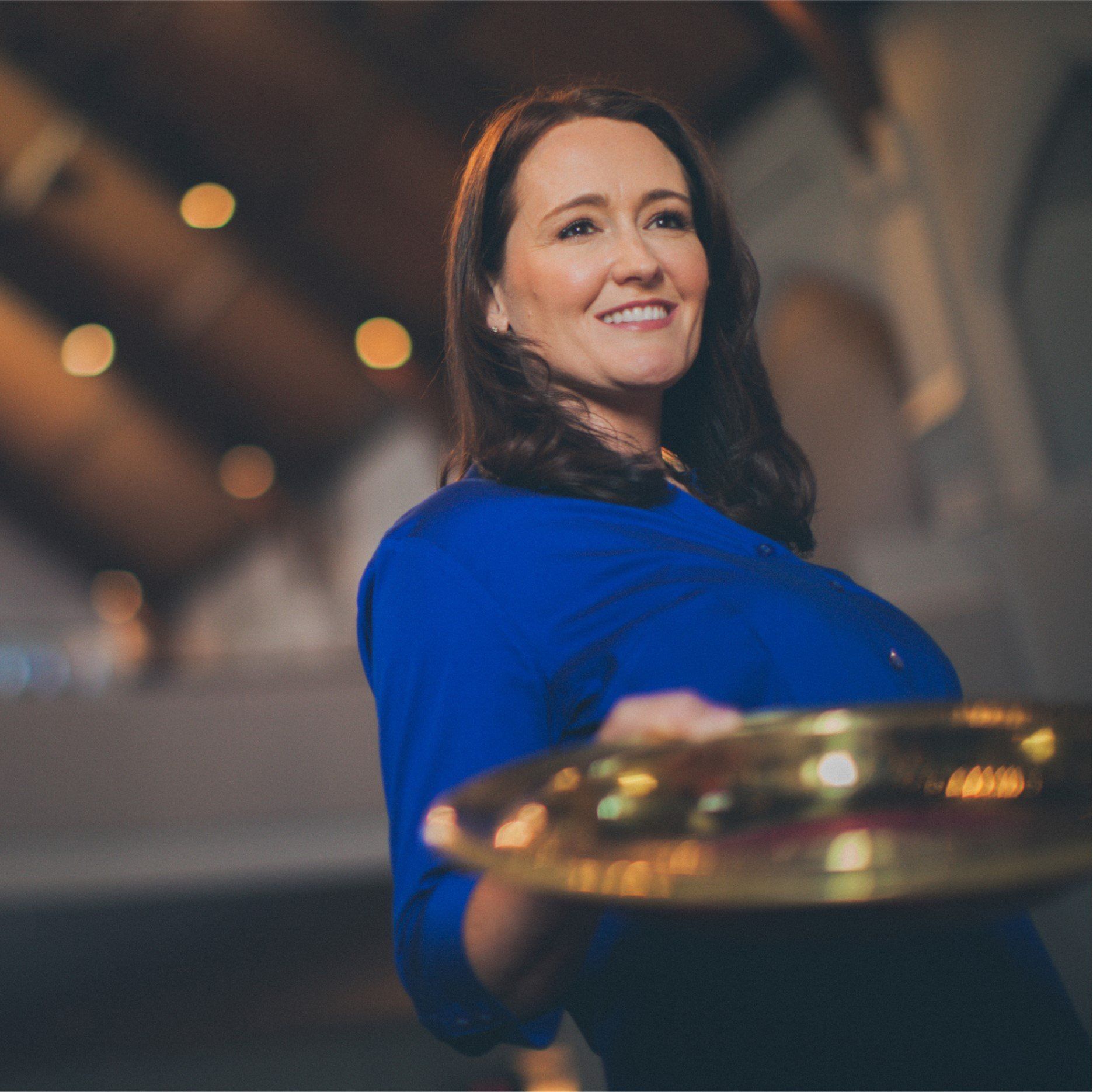 A woman in a blue shirt is holding a cymbal and smiling