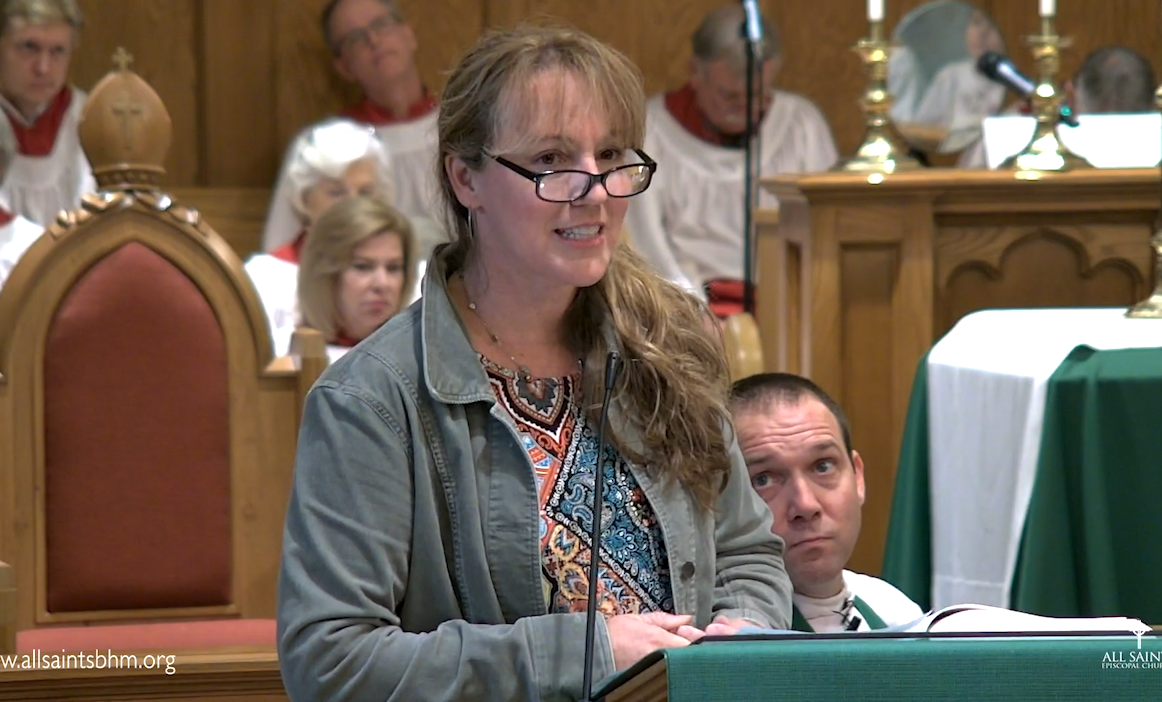 A woman wearing glasses is standing at a podium in a church.
