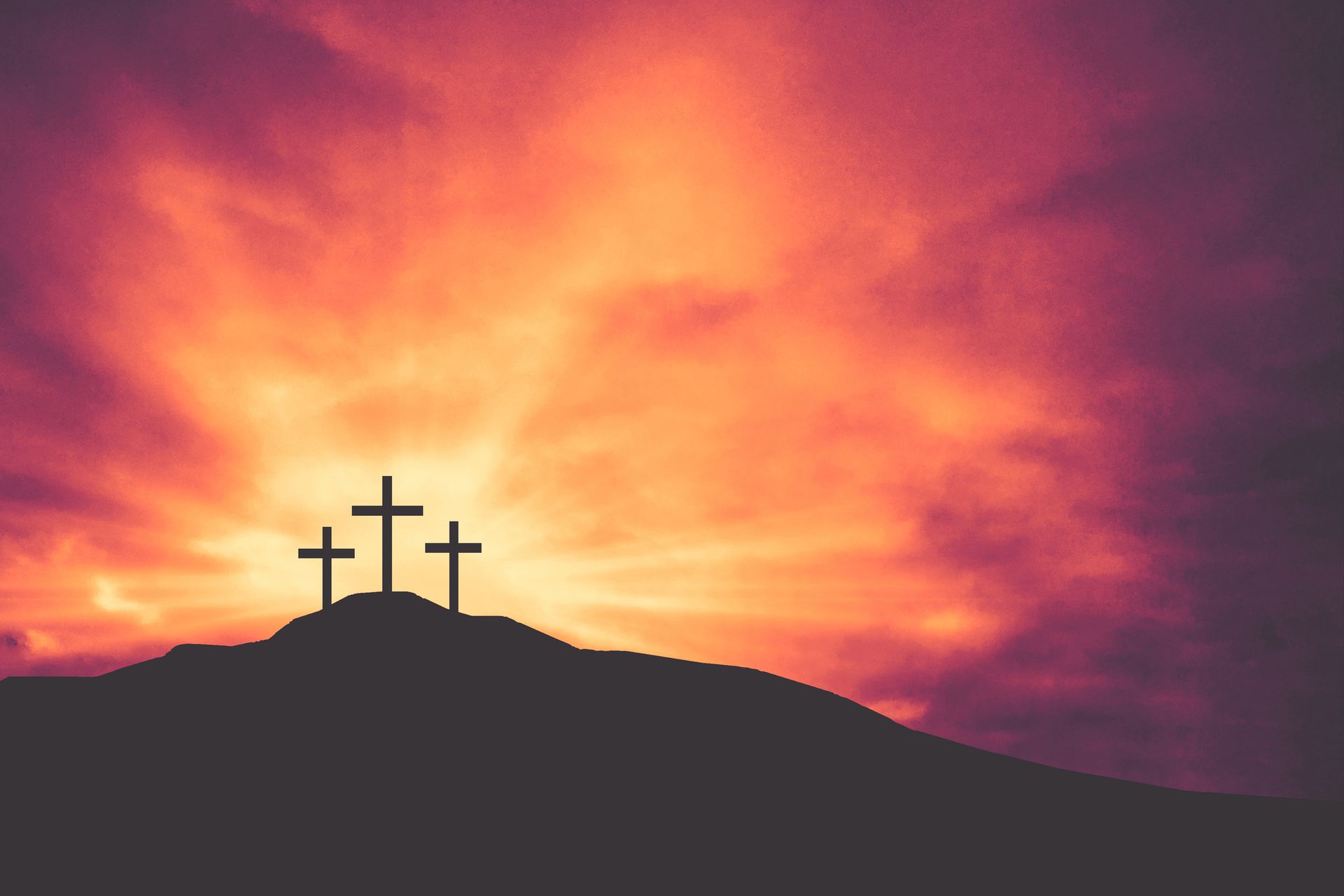 Three crosses on top of a hill at sunset.