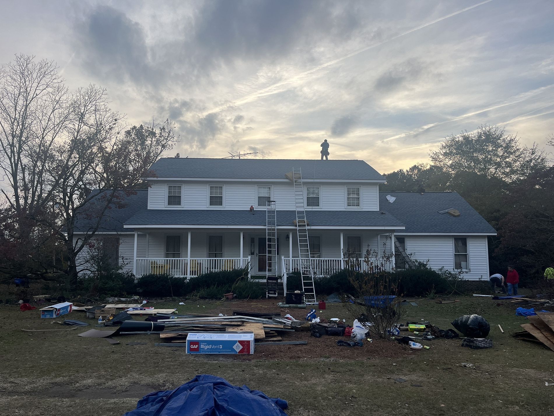 A white house under renovation with scaffolding on the front porch and debris scattered across the yard.