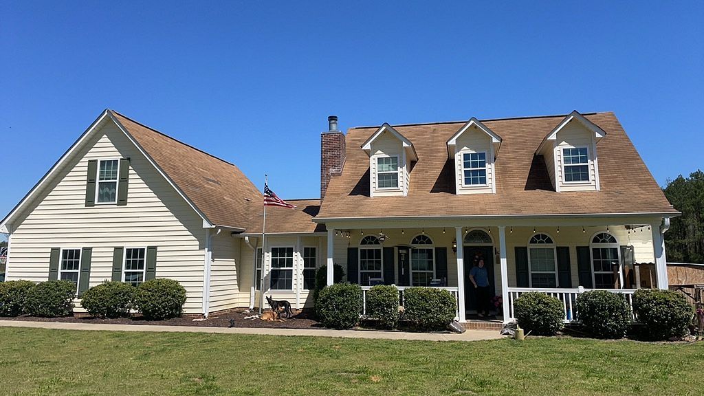 A white house with a brown roof and a large porch