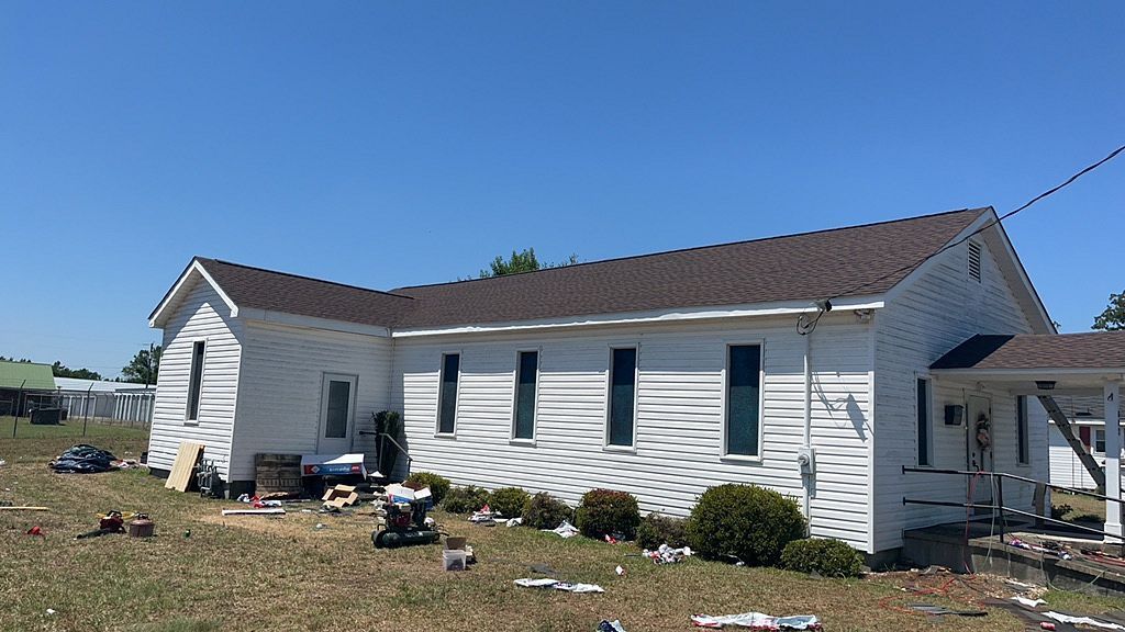 A white house with a brown roof is sitting in the middle of a field.
