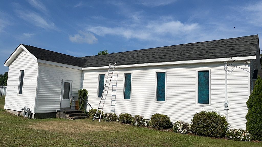 A white house with blue windows and a black roof is sitting on top of a lush green field.